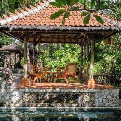 Ein traditionelles balinesisches Pavillon mit Holzstühlen und Tisch, umgeben von üppigem Grün und tropischen Pflanzen.