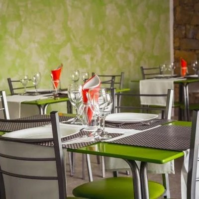 Ein modernes Restaurant mit grün-braunen Wänden hat Tische mit weißen Tischdecken und bunten Servietten aufgestellt.