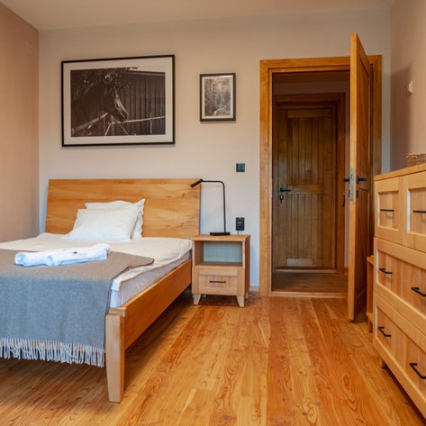 Ein gemütliches Schlafzimmer mit einem Holzbett, einer grauen Decke und einem Nachttisch, der eine Lampe trägt.