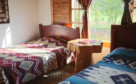 Ein gemütliches Zimmer mit zwei Betten, die mit bunten Decken bedeckt sind, und einem rustikalen Holztisch in der Mitte.