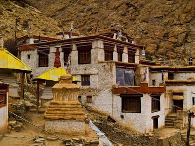 Eine traditionelle tibetische Klosteranlage mit gelben Dächern und Stupas, umgeben von steilen Felsen und Gebetsfahnen.
