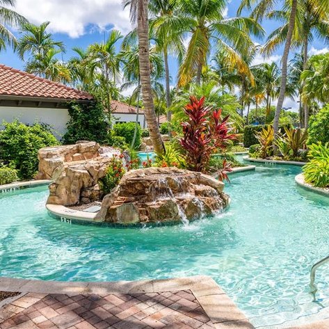 Ein einladender Poolbereich mit klarem Wasser, umgeben von üppigen Palmen und bunten Pflanzen, ideal für Entspannung.