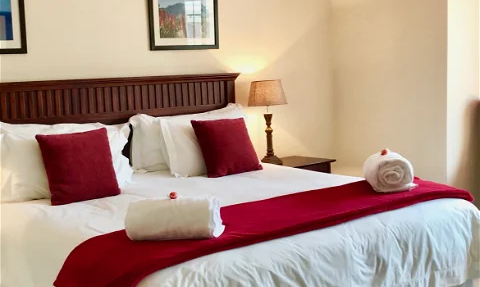 Ein gemütliches Schlafzimmer mit einem großen Bett, roten Kissen und einem warmen Licht von einer Tischlampe.