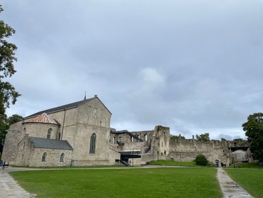 Eine alte Kirche mit einem kupfernen Dach und einer beeindruckenden Ruine im Hintergrund, umgeben von grünem Gras.