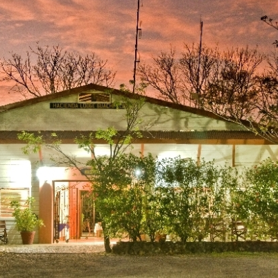Ein rustikales Hotelgebäude mit einem einladenden Eingang, umgeben von üppigem Grün und einem malerischen Abendhimmel.