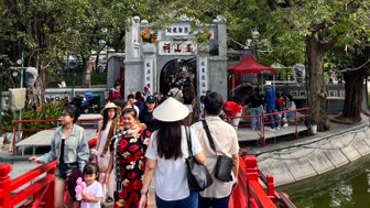 Eine belebte Brücke führt zu einem Tor, umgeben von Bäumen und Menschen, die die Atmosphäre genießen.
