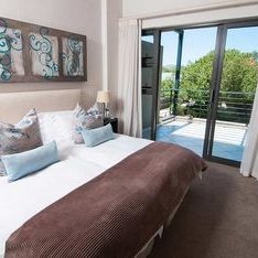 Ein helles Schlafzimmer mit einem großen Doppelbett, dekoriert mit bunten Kissen und einem modernen Kunstwerk an der Wand.