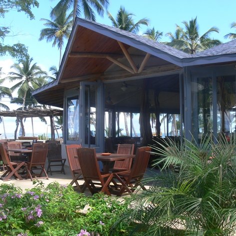 Ein einladendes Restaurant mit Holzstühlen und Tischen, umgeben von Palmen und bunten Blumen, direkt am Strand.
