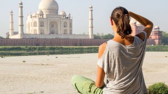Eine Person sitzt am Ufer und betrachtet das majestätische Taj Mahal, umgeben von einer ruhigen Landschaft.