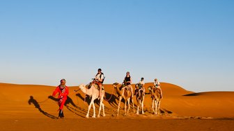 Familie zieht gemeinsam mit einer Kamelkarawane durch die Wüstenlandschaft der Sahara – Familienreise nach Marokko