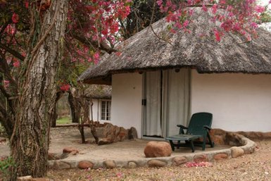 Eine gemütliche Hütte mit einem Strohdach, umgeben von bunten Bougainvillea-Blüten und einem einladenden Sitzbereich.