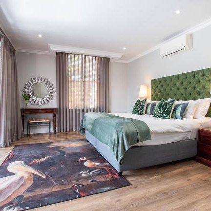 Ein elegantes Schlafzimmer mit einem großen Bett, grüner Bettwäsche und einem kunstvollen Teppich mit Vogelmotiven.