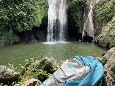 Ein beeindruckender Wasserfall stürzt in einen klaren, grünen Teich, umgeben von üppigem, grünem Laub und Felsen.