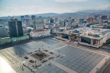 Ein Blick auf den Sukhbaatar-Platz in Ulaanbaatar, umgeben von modernen Gebäuden und sanften Hügeln im Hintergrund.