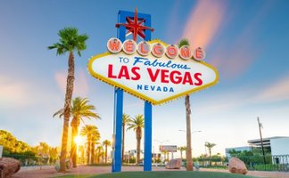 Das berühmte Willkommensschild von Las Vegas strahlt in leuchtenden Farben, umgeben von Palmen und einem klaren Himmel.