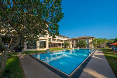 Ein klarer Pool spiegelt die Sonne wider, umgeben von modernen Gebäuden und üppigem Grün im Mirissa Mandara Resort.