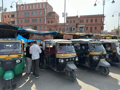 Eine belebte Straße in Jaipur, gesäumt von bunten Rikschas und Menschen, die an einem Stand mit Blumen dekorieren.