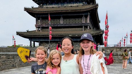 Vier Mädchen stehen fröhlich vor einem historischen Torturm in Xi'an und lächeln in die Kamera, während bunte Laternen im Hintergrund schweben.