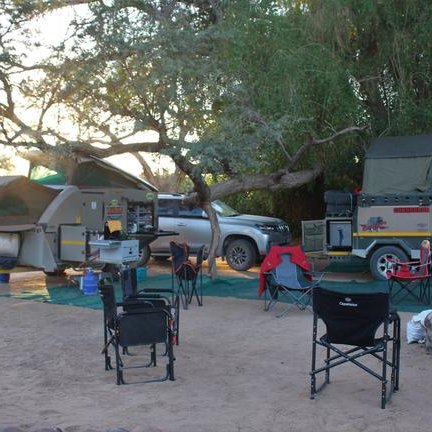 Ein Campingplatz mit mehreren Wohnwagen und Stühlen, umgeben von Bäumen und sanftem Licht der Abenddämmerung.
