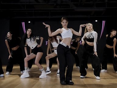 Eine Gruppe von Tänzerinnen in sportlicher Kleidung führt synchronisierte Bewegungen in einem modernen Tanzstudio aus.