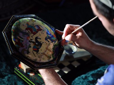 Ein Künstler malt sorgfältig auf einer runden, bemalten Oberfläche mit lebendigen Farben und detaillierten Szenen.