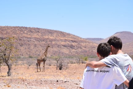Zwei Kinder beobachten aus der Ferne eine Giraffe - Namibia Rundreise mit Kindern