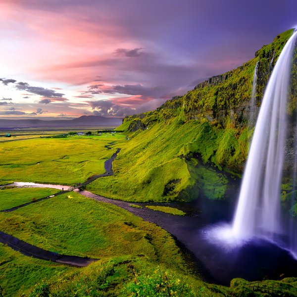Ein majestätischer Wasserfall stürzt über grüne Klippen, während der Himmel in sanften Pastellfarben leuchtet.