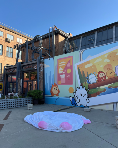 Eine große, weiße Decke mit rosa Details liegt auf dem Boden vor einer bunten Wandmalerei mit cartoonhaften Tieren.