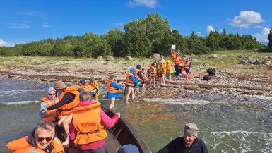 Eine Gruppe von Menschen in orangefarbenen Schwimmwesten steht am Ufer, während ein Boot im Wasser liegt.