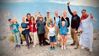 Reisegruppe posiert gemeinsam mit ihrem Guide vor der Bergkulisse des Jebel Shams – Oman Reise mit Kindern
