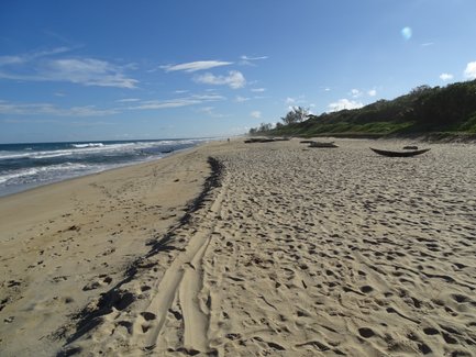 Ein ruhiger Strand mit sanften Wellen, Fußabdrücken im Sand und traditionellen Booten, die am Ufer liegen.