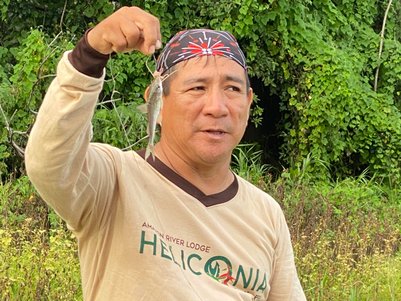 Ein Mann hält stolz einen gefangenen Fisch in der Hand, umgeben von üppigem, grünem Dschungel im Amazonasgebiet.