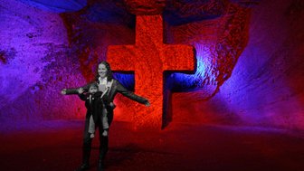 Eine Frau steht mit einem Kind in einem farbenfrohen Salzraum, hinter ihnen leuchtet ein großes rotes Kreuz.