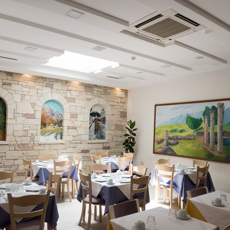 Ein eleganter Restaurantbereich mit Holztischen, blauen Tischdecken und beeindruckenden Wandmalereien, die ländliche Szenen zeigen.