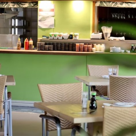 Ein einladendes Restaurant mit hellgrünen Wänden, Tischen aus Holz und einem gut sortierten Buffet im Hintergrund.
