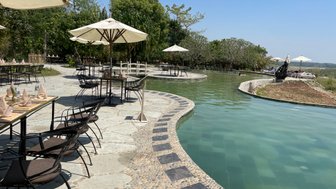 Ein einladender Poolbereich mit Sonnenschirmen und Tischen, umgeben von üppigem Grün und klarem Himmel.