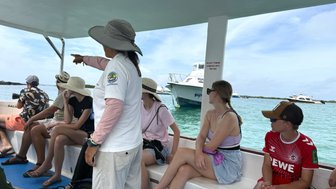 Eine Gruppe von Touristen sitzt auf einem Boot, während eine Führerin auf etwas im Wasser zeigt.