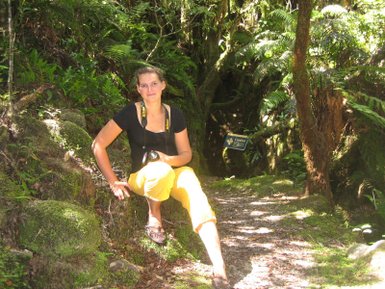 Eine Frau sitzt auf einem moosbedeckten Steinweg im Wald, umgeben von üppigem Grün und tropischen Pflanzen.