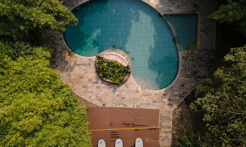 Ein Blick von oben auf einen eleganten Pool, umgeben von üppigem Grün und einem kleinen Wasserfall mit Pflanzen.