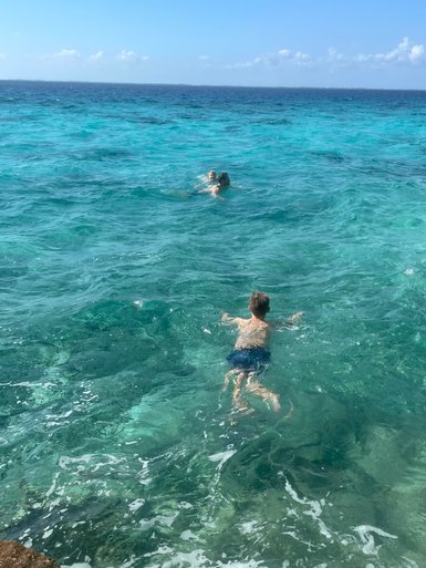 Zwei Kinder schwimmen fröhlich im klaren, türkisfarbenen Wasser unter einem strahlend blauen Himmel.