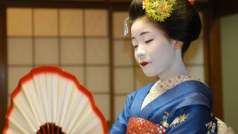 Eine Geisha in traditioneller Kleidung hält einen Fächer und zeigt eine nachdenkliche Miene in einem japanischen Raum.