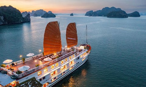 Ein traditionelles Schiff mit roten Segeln gleitet sanft über das ruhige Wasser der Halong-Bucht, umgeben von beeindruckenden Felsen.