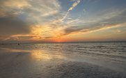 Ein atemberaubender Sonnenuntergang über dem ruhigen Meer, mit sanften Wellen und einem goldenen Himmel voller Wolken.