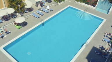 Ein klarer Pool mit sanften Wellen und einer Treppe, umgeben von Liegen und Sonnenschirmen, ideal für Entspannung.