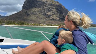 Eine Mutter sitzt auf einem Boot und umarmt ihre beiden Kinder, während sie die Aussicht auf die grüne Lagune genießen.