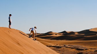 Kinder sausen mit Sandboards die hohen Dünen der Wüste hinunter – Marokko Familienreise
