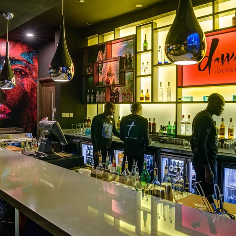 Im eleganten Dawa Lounge in Nairobi stehen Barkeeper hinter einer stilvollen Bar mit bunten Getränken und einer beeindruckenden Wandkunst.