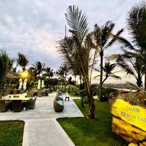 Ein einladender Strandbereich mit Palmen, gemütlichen Sitzgelegenheiten und einem Schild, das die Cham Beach Bar anzeigt.