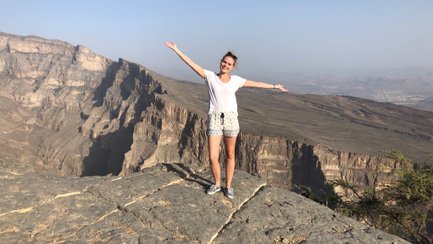 Eine Frau steht auf einem Felsen und breitet die Arme aus, während sie die beeindruckende Berglandschaft genießt.