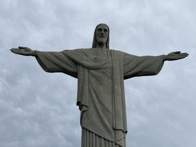Die Christusstatue erhebt sich majestätisch mit ausgebreiteten Armen unter einem bewölkten Himmel.